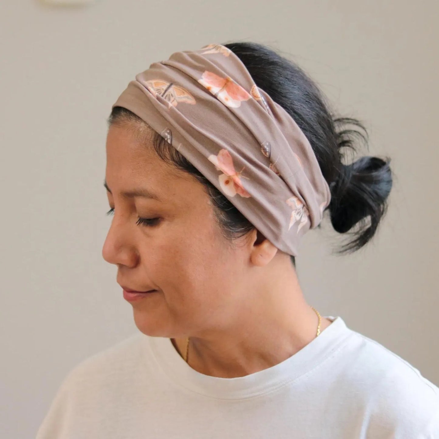 Woman wearing a beige headband with butterfly print patterns on a plain background