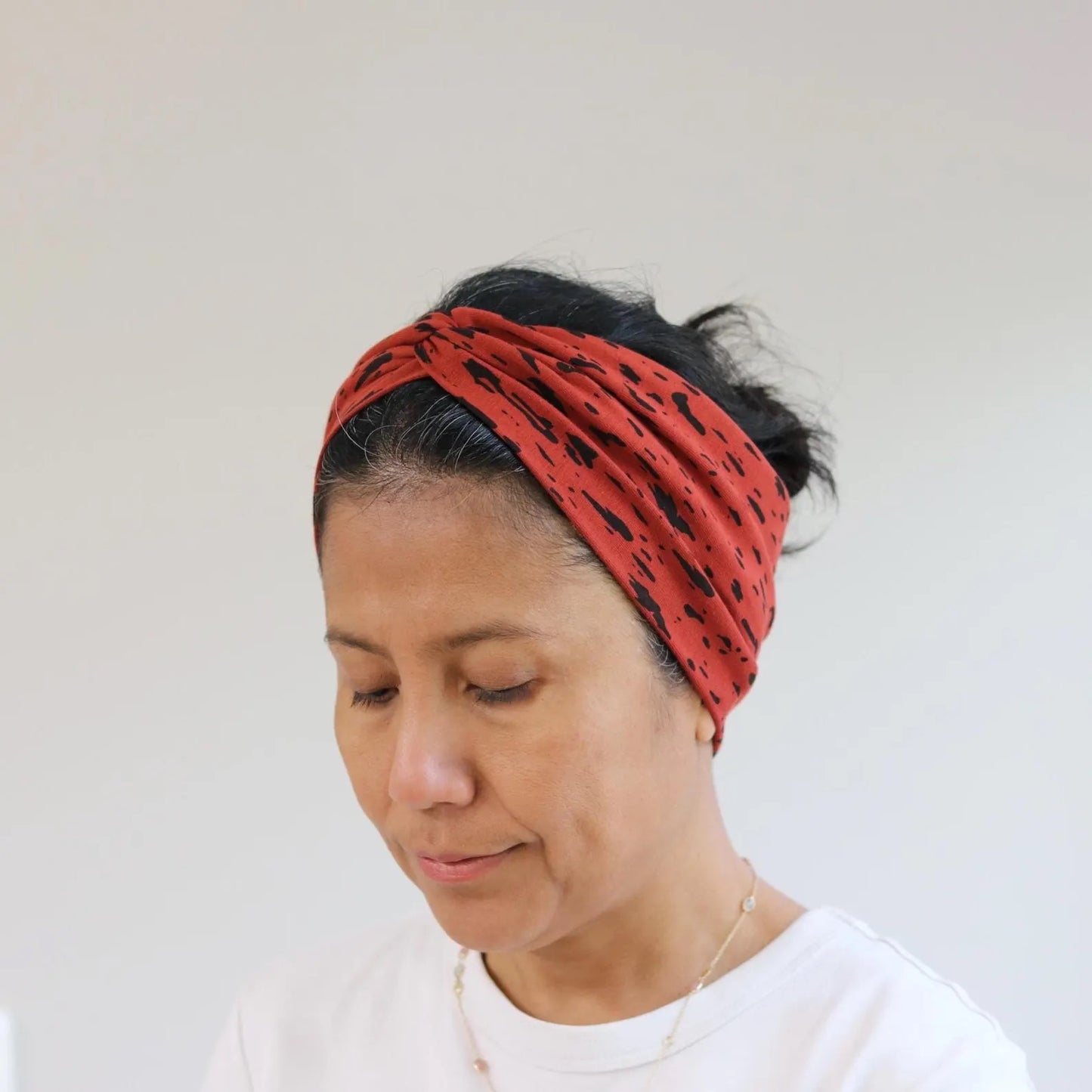 Woman wearing a red headband with black patterns against a plain background