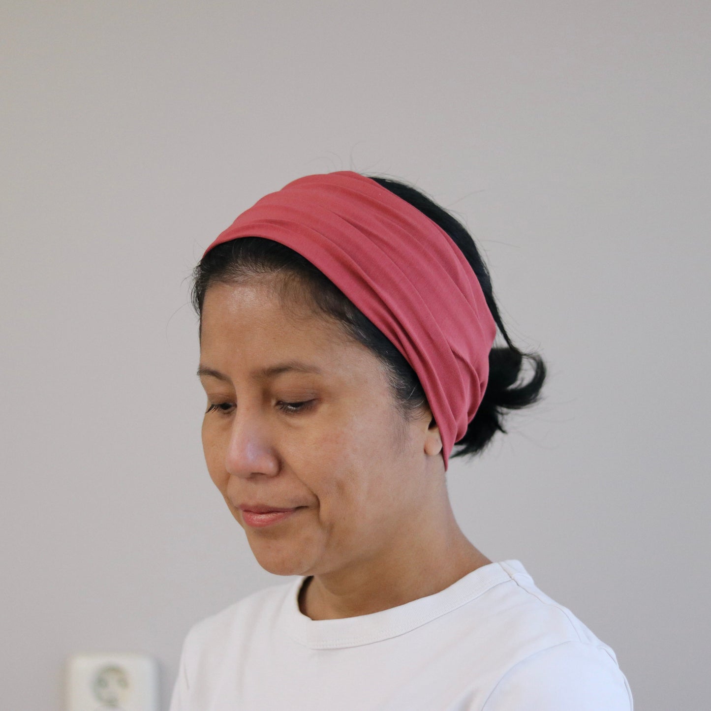 Woman wearing a pink headscarf and white shirt against a plain background