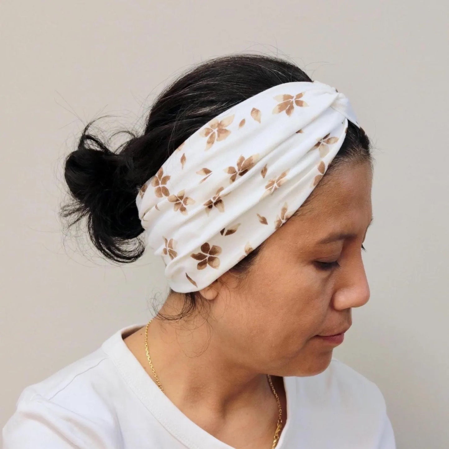 Woman wearing a white headband with brown floral pattern on a plain background