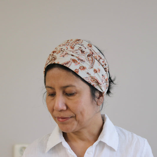 Woman wearing a floral headscarf and white shirt against a plain background