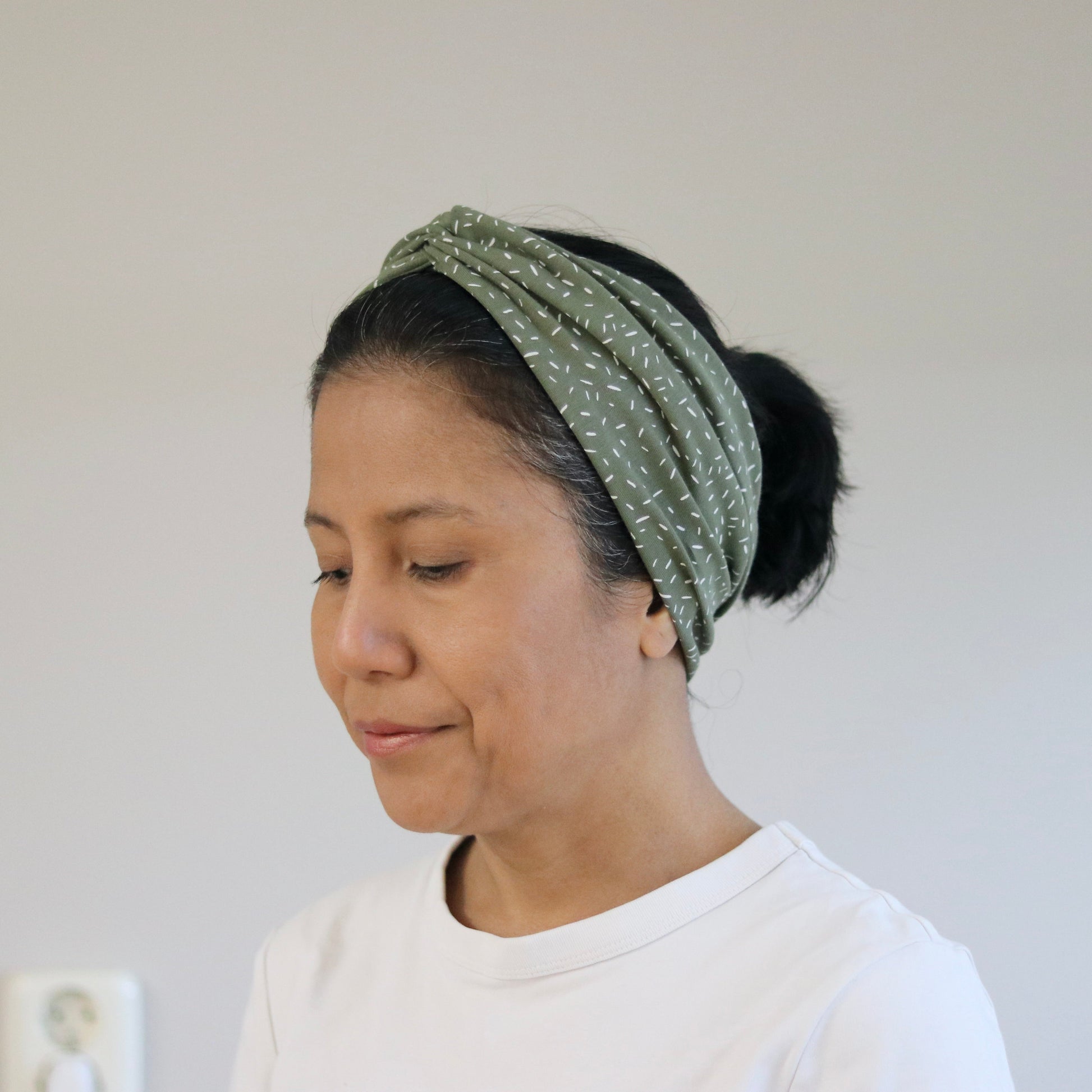 Woman wearing a green headband with white polka dots against a plain background