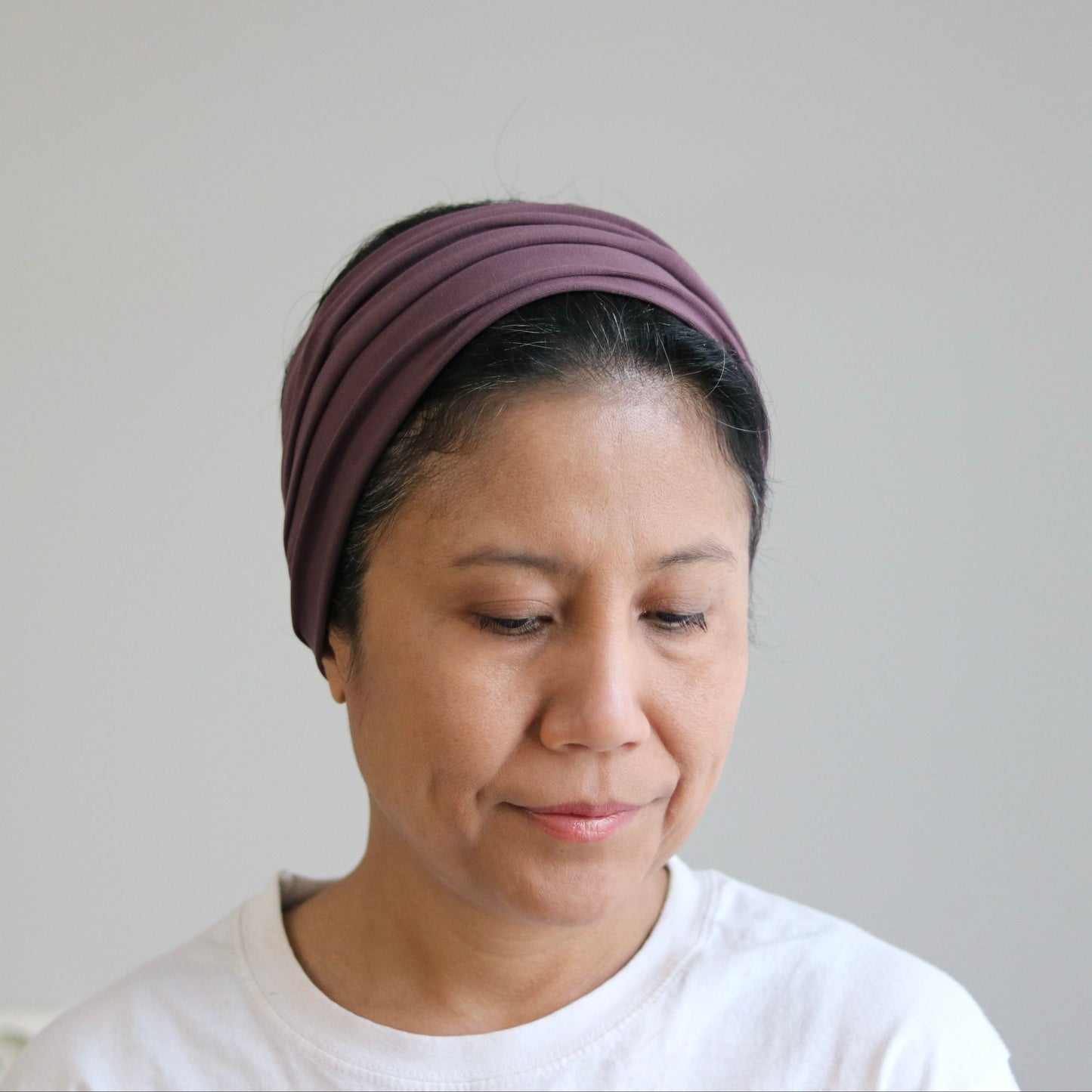 Woman wearing a purple headscarf against a plain background
