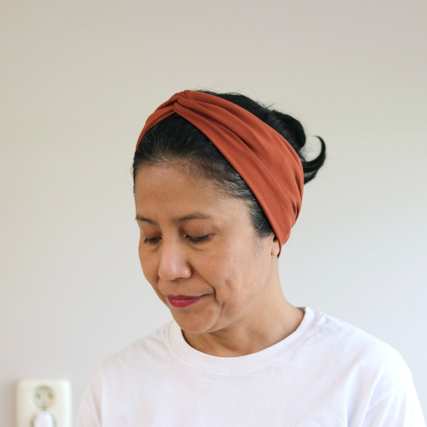 Woman wearing a rust-colored headband against a plain background