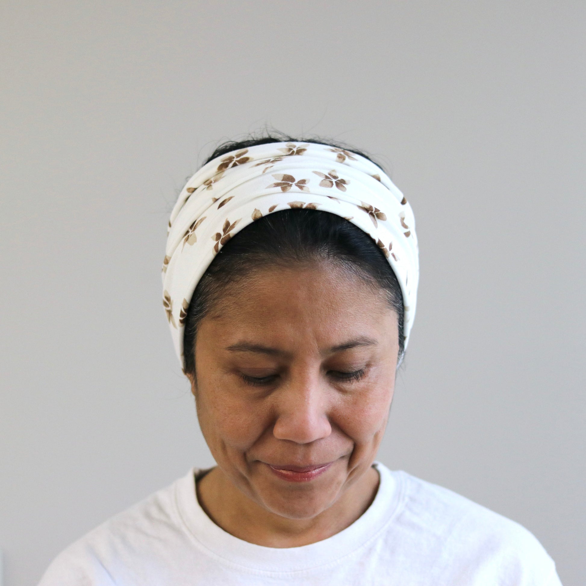 Woman wearing a white headscarf with a pattern against a plain background