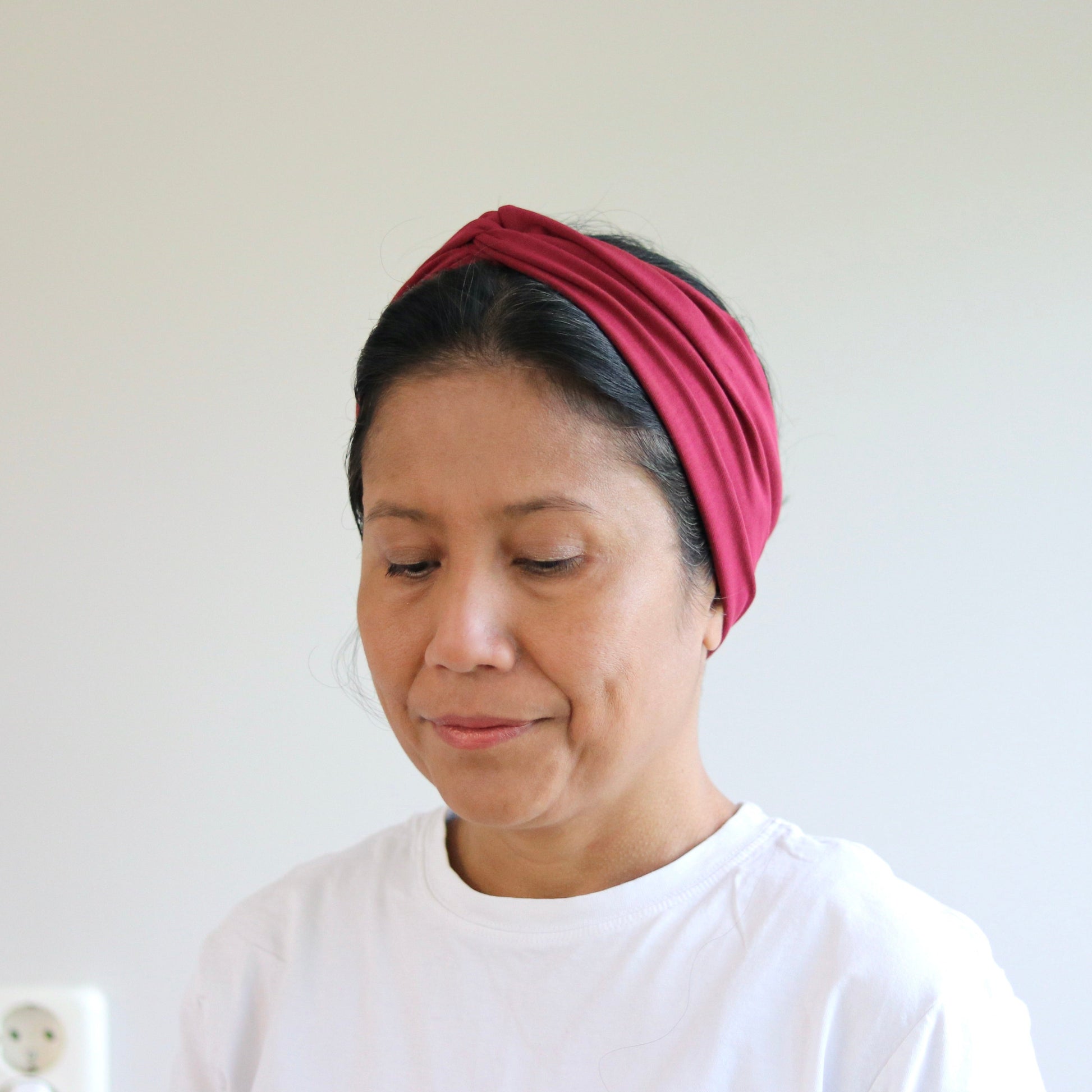 Woman wearing a bordeaux headband against a plain background