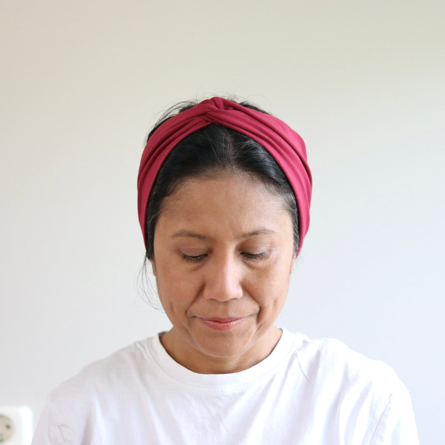 Woman wearing a bordeaux headband and white shirt against a plain background