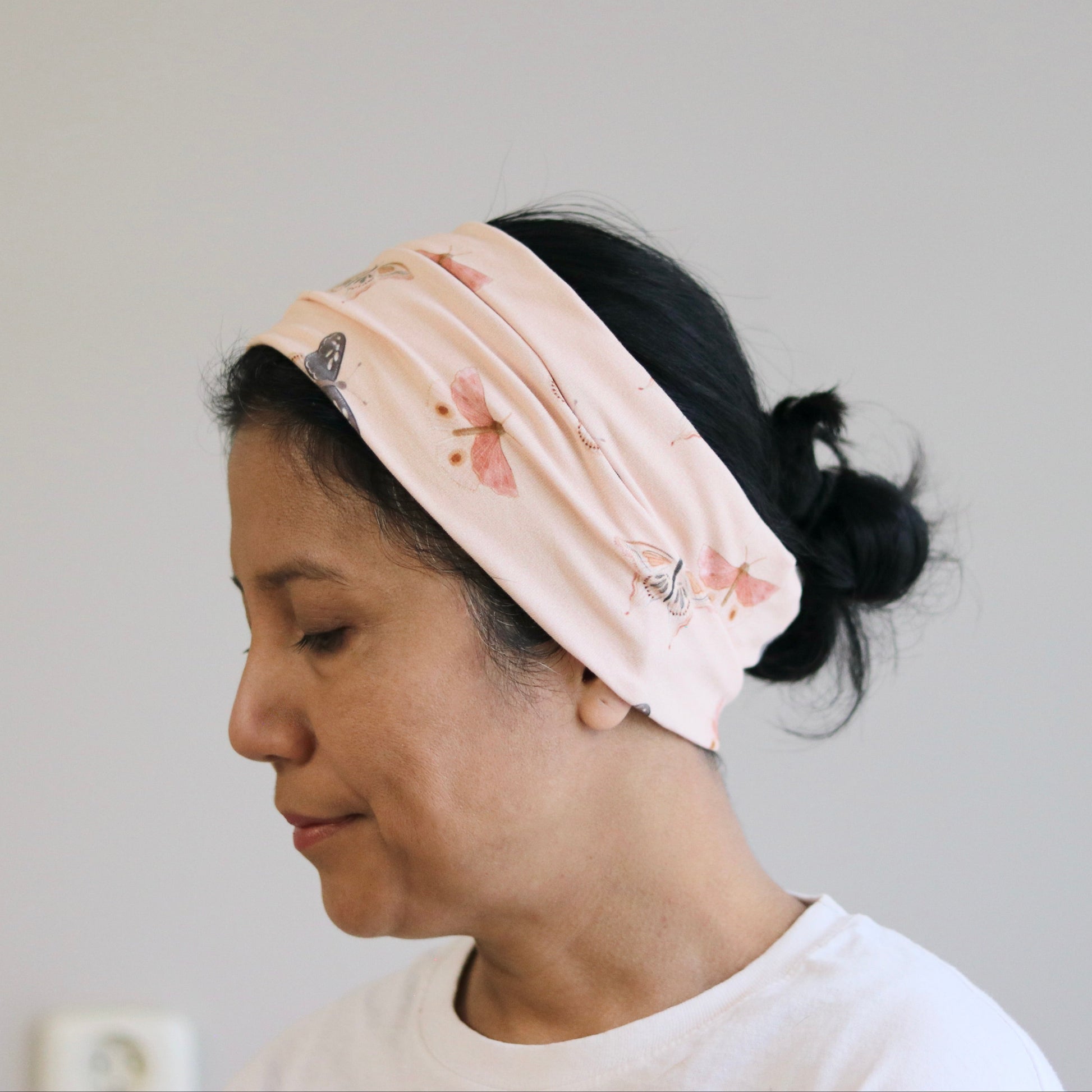 Woman wearing a light pink headband with floral patterns against a plain background