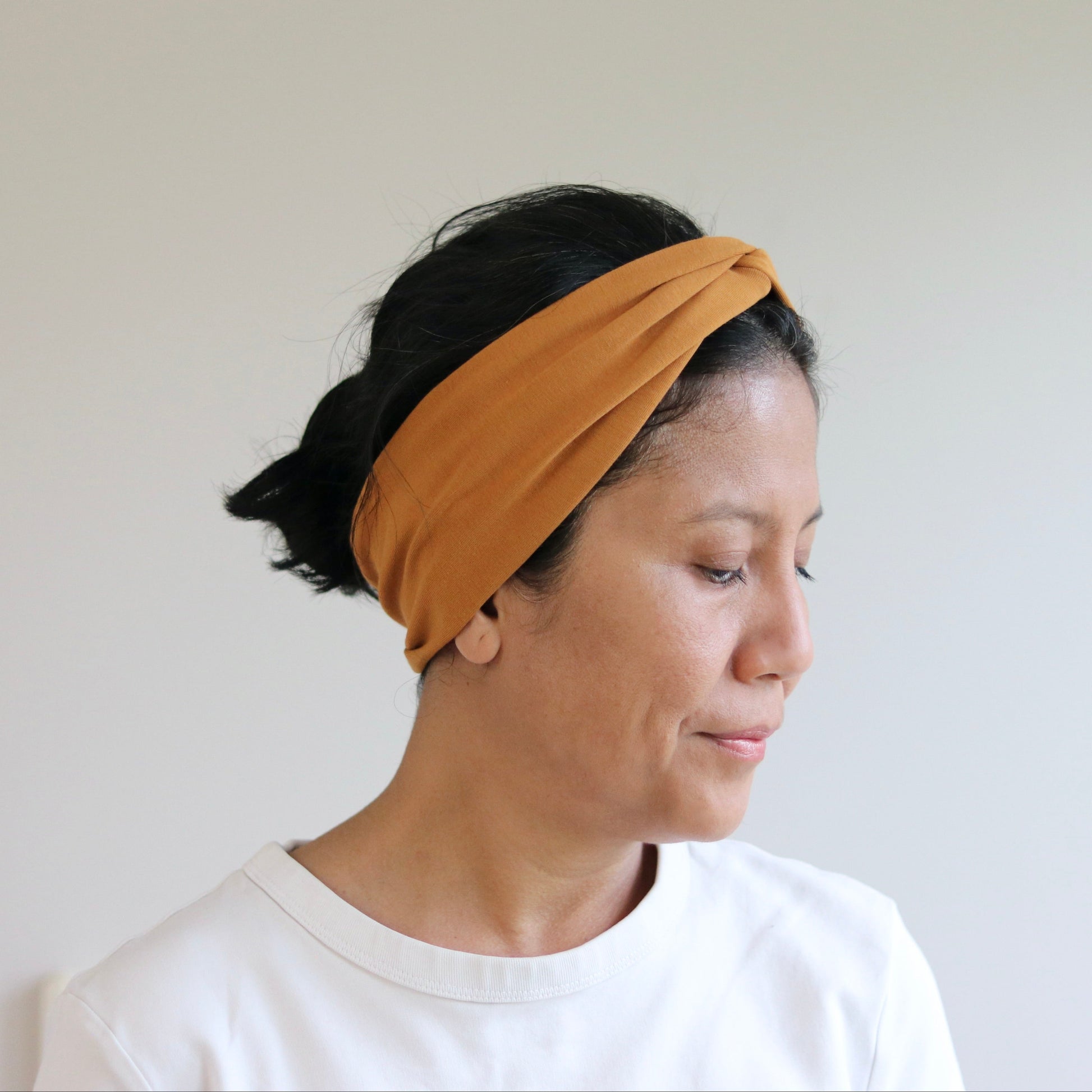 Woman wearing a mustard yellow headband against a plain background