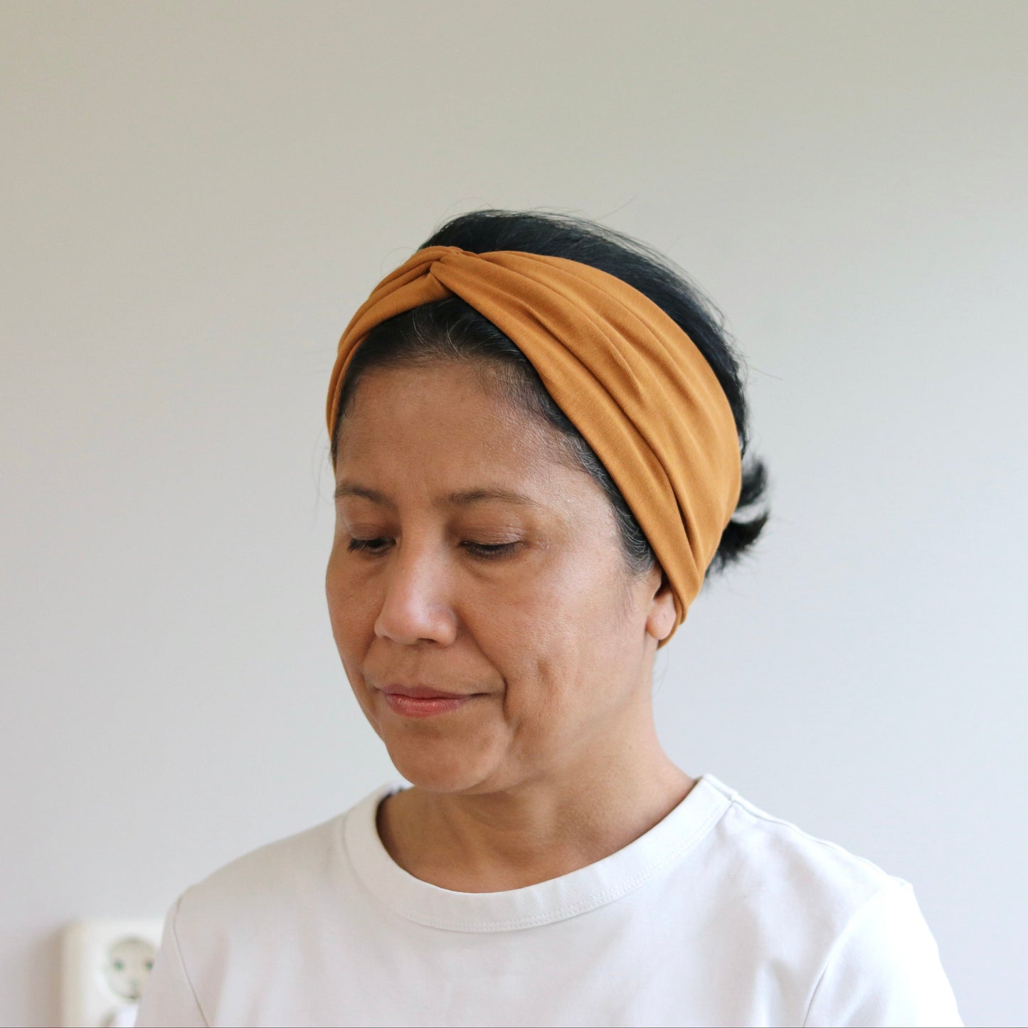 Woman wearing a mustard yellow headband against a plain background