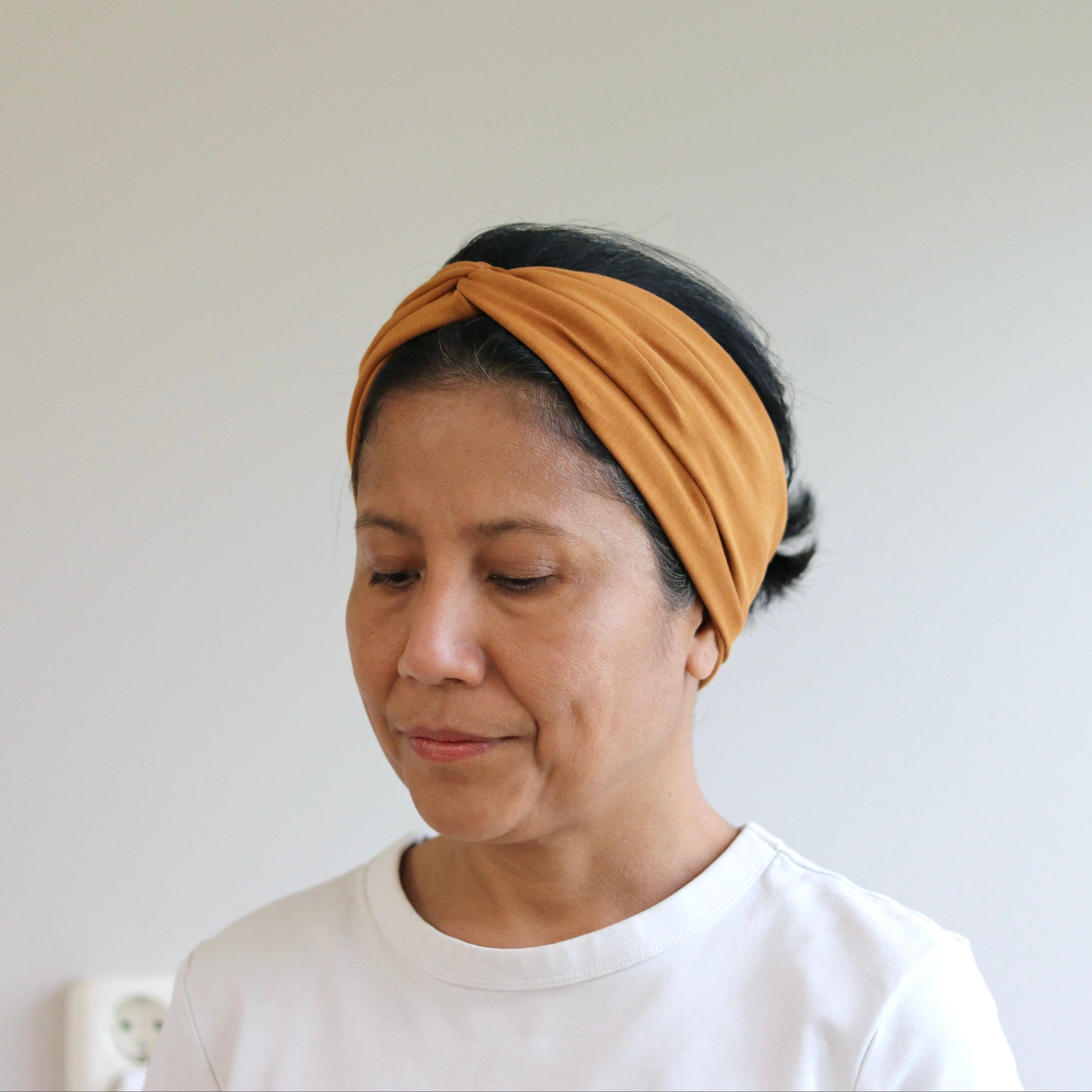 Woman wearing a mustard yellow headband against a plain background