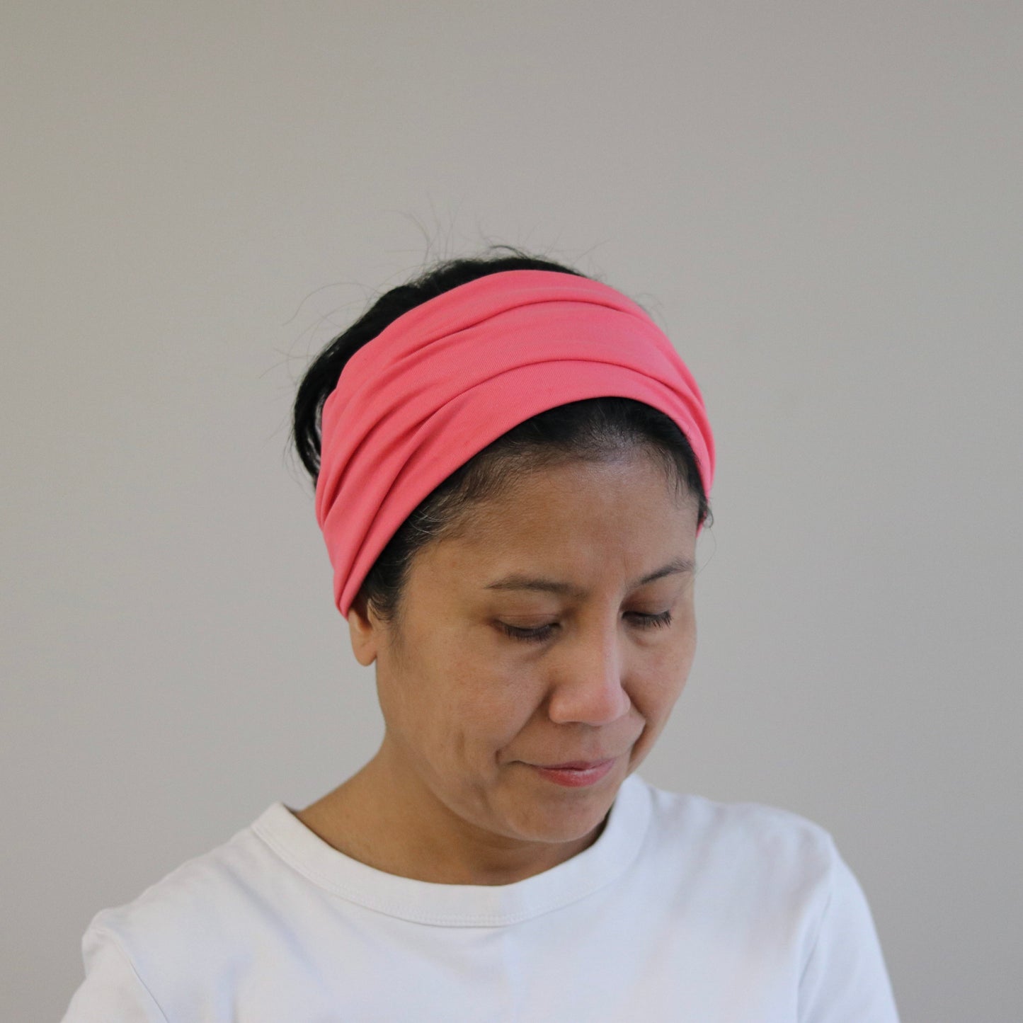 Woman wearing an coral pink headband against a plain background