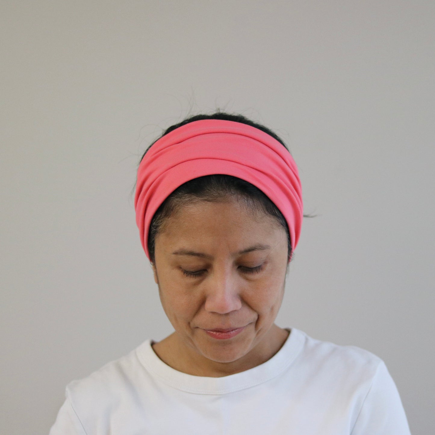 Person wearing an coral- pink headband against a plain background
