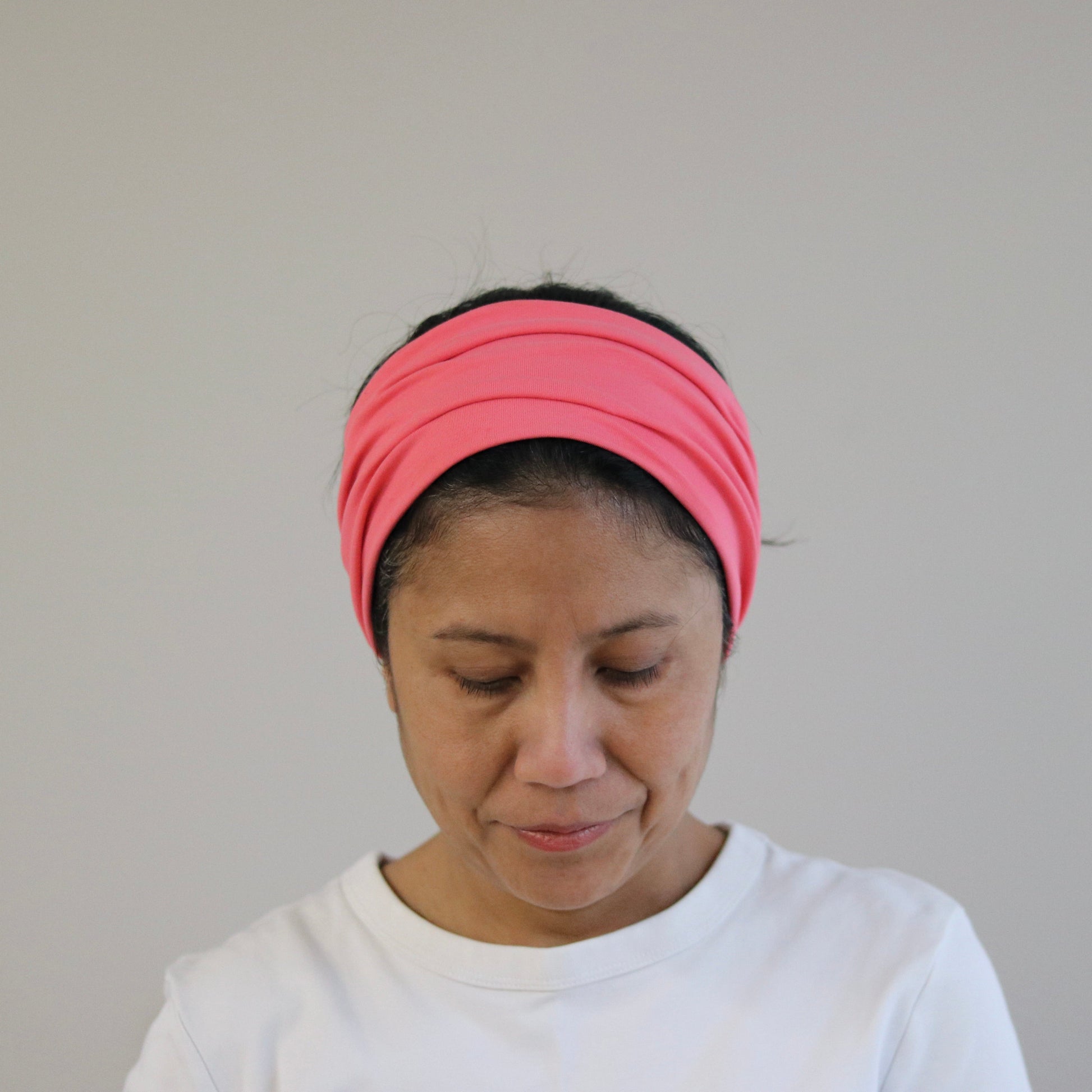 Person wearing an coral- pink headband against a plain background