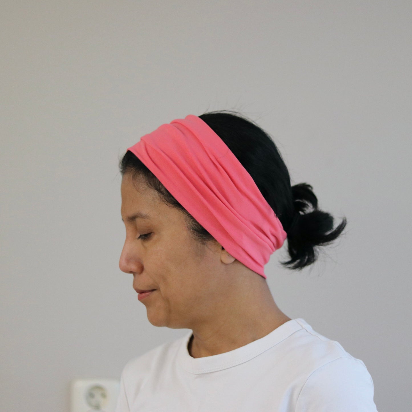 Person wearing an coral- pink headband against a plain background
