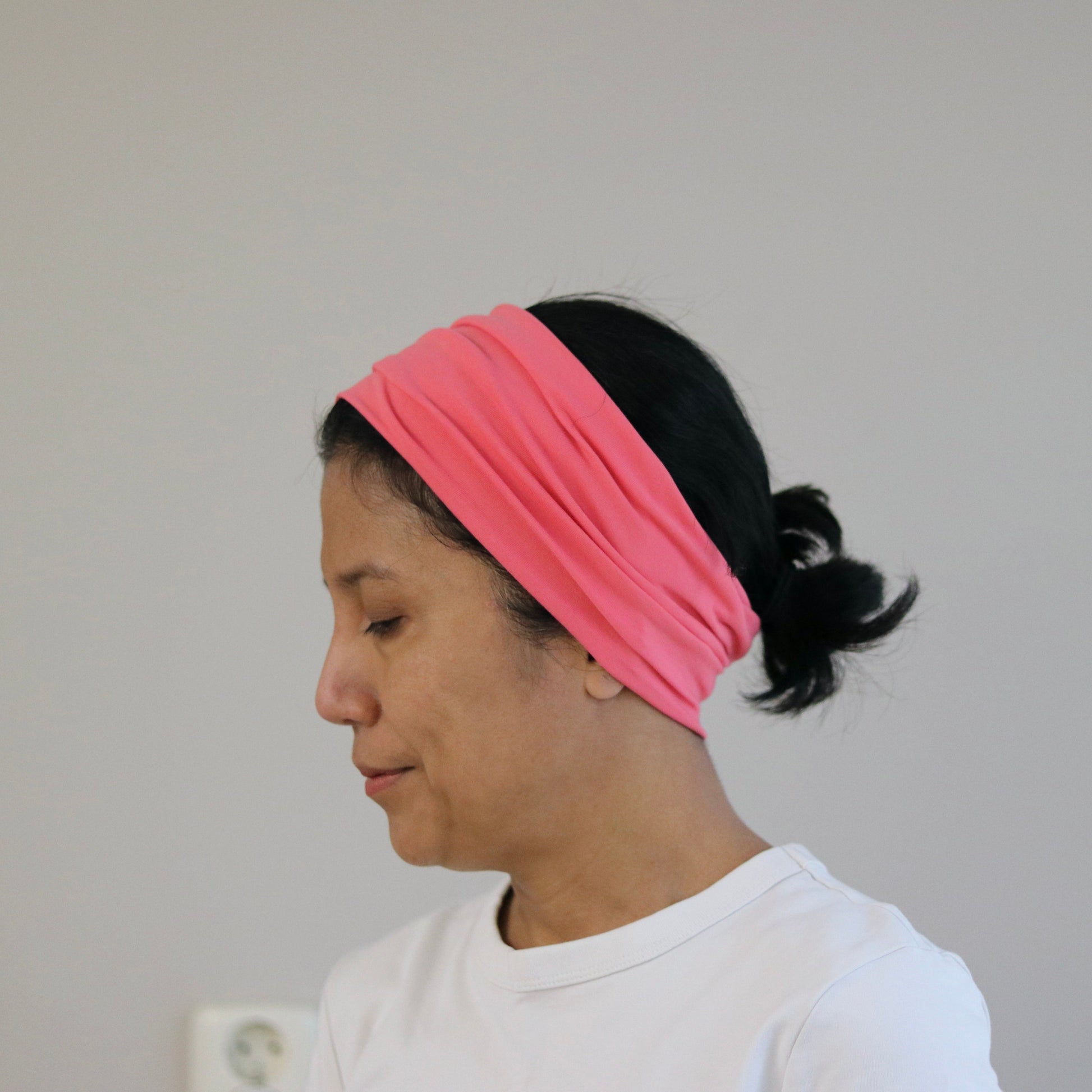 Person wearing an coral- pink headband against a plain background