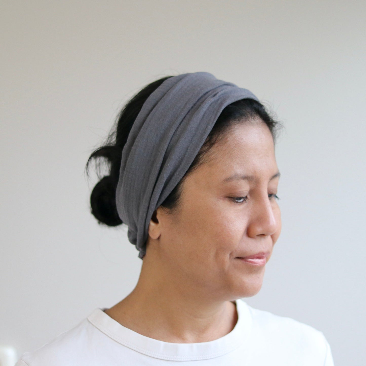 A woman wearing a gray fabric headband, shown in profile against a plain light gray wall.