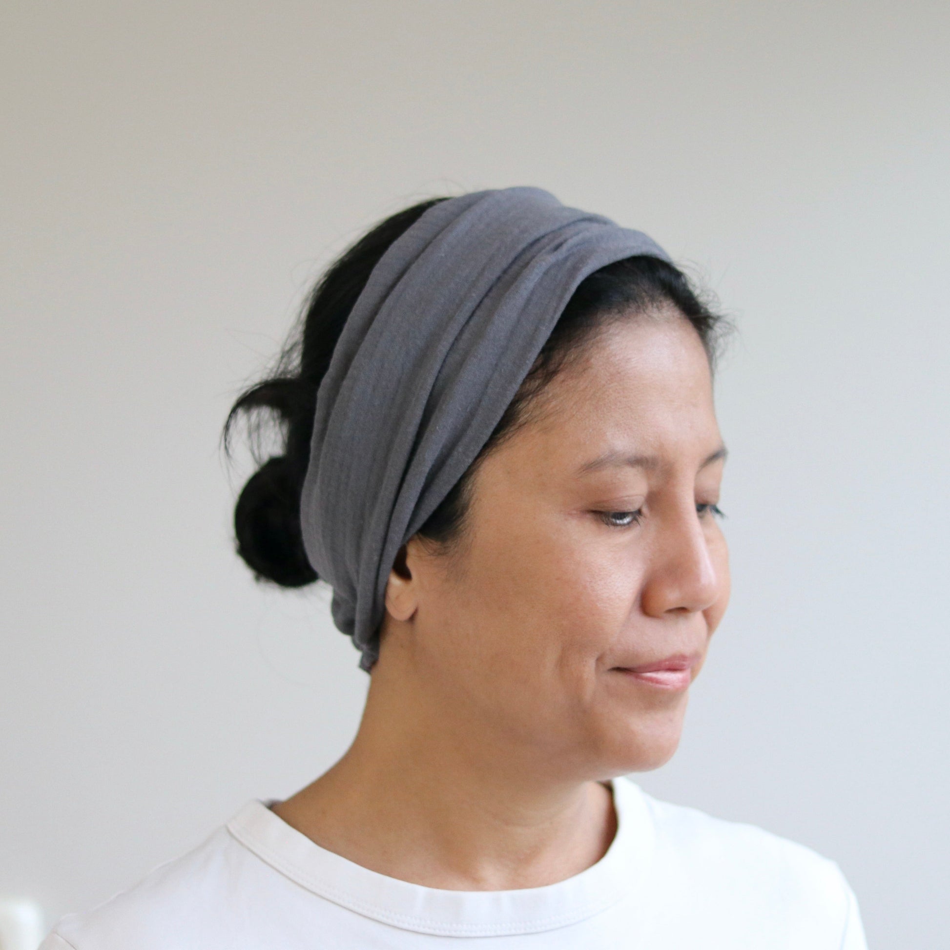 A woman wearing a gray fabric headband, shown in profile against a plain light gray wall.