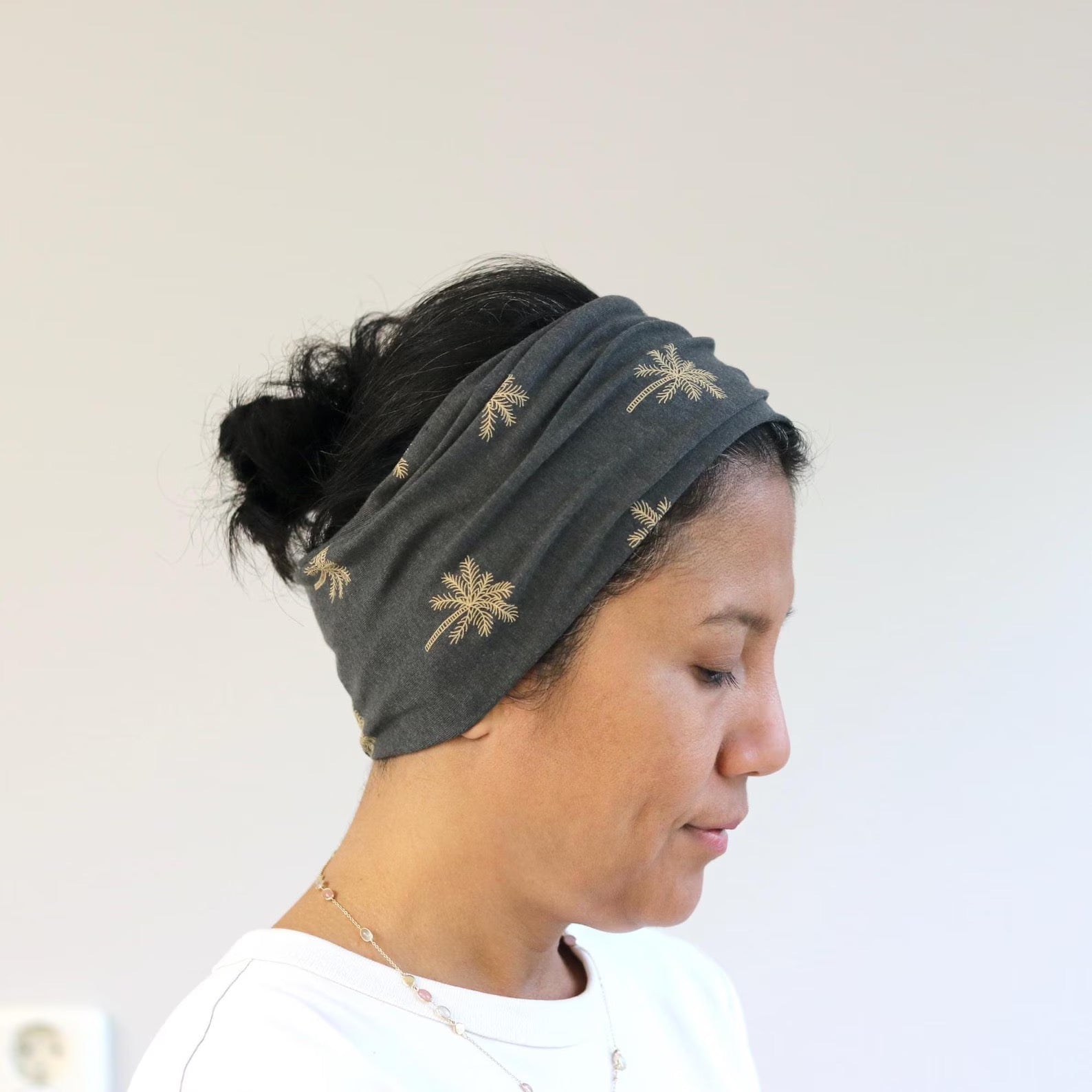 Woman wearing a dark gray headband with gold palm tree designs on a plain background