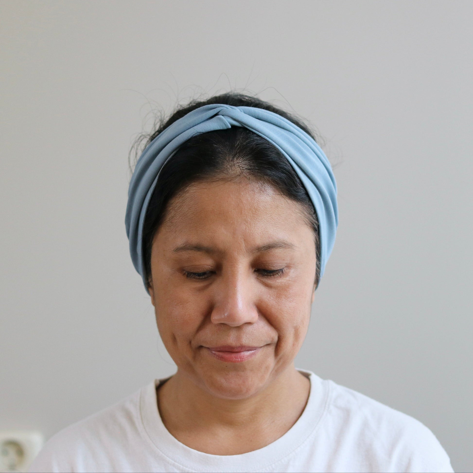 Woman wearing a dusty- blue headband against a plain background