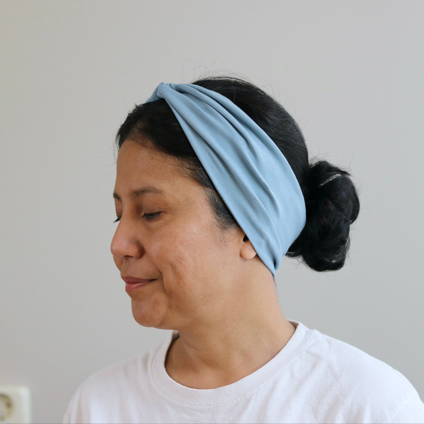 Woman wearing a dusty-  blue headband against a plain background