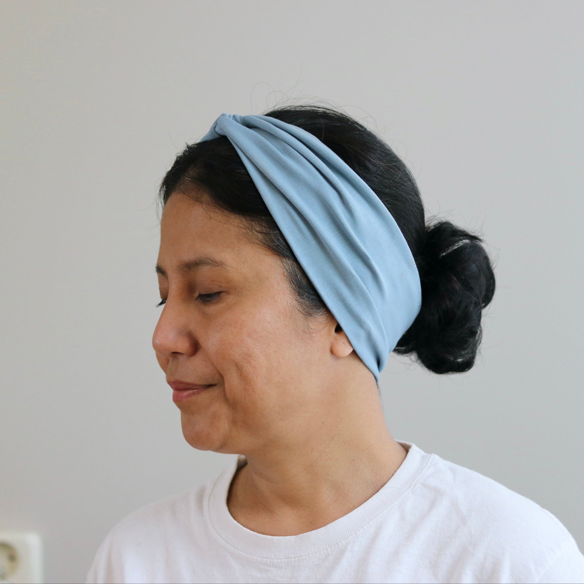 Woman wearing a dusty-  blue headband against a plain background