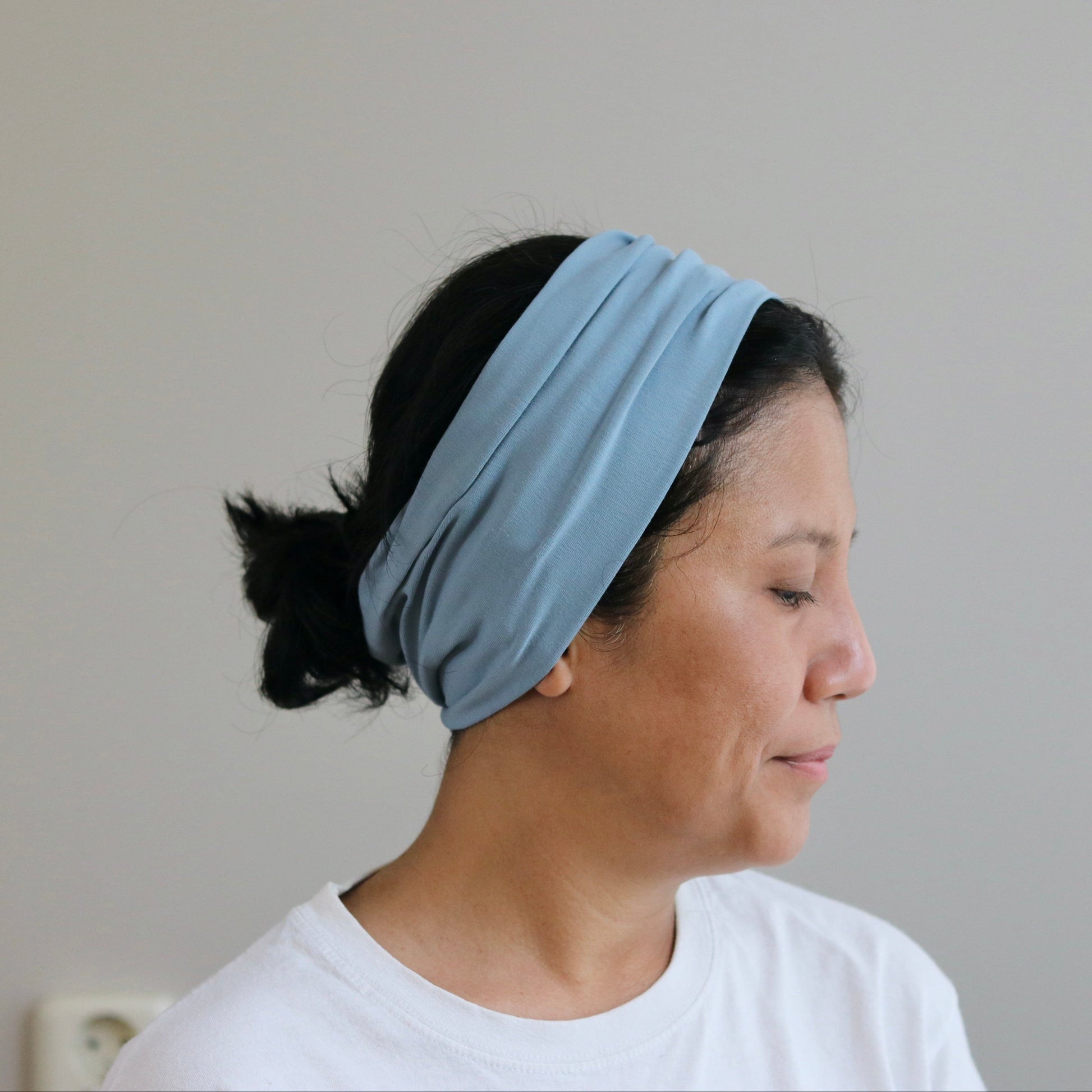 Woman wearing a dusty- blue headband against a plain background