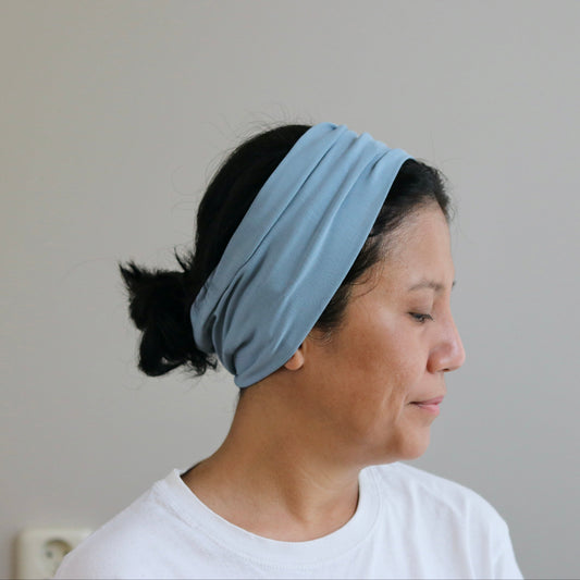 Woman wearing a dusty- blue headband against a plain background