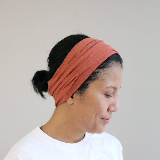 Woman wearing a dusty- terra headband against a plain background