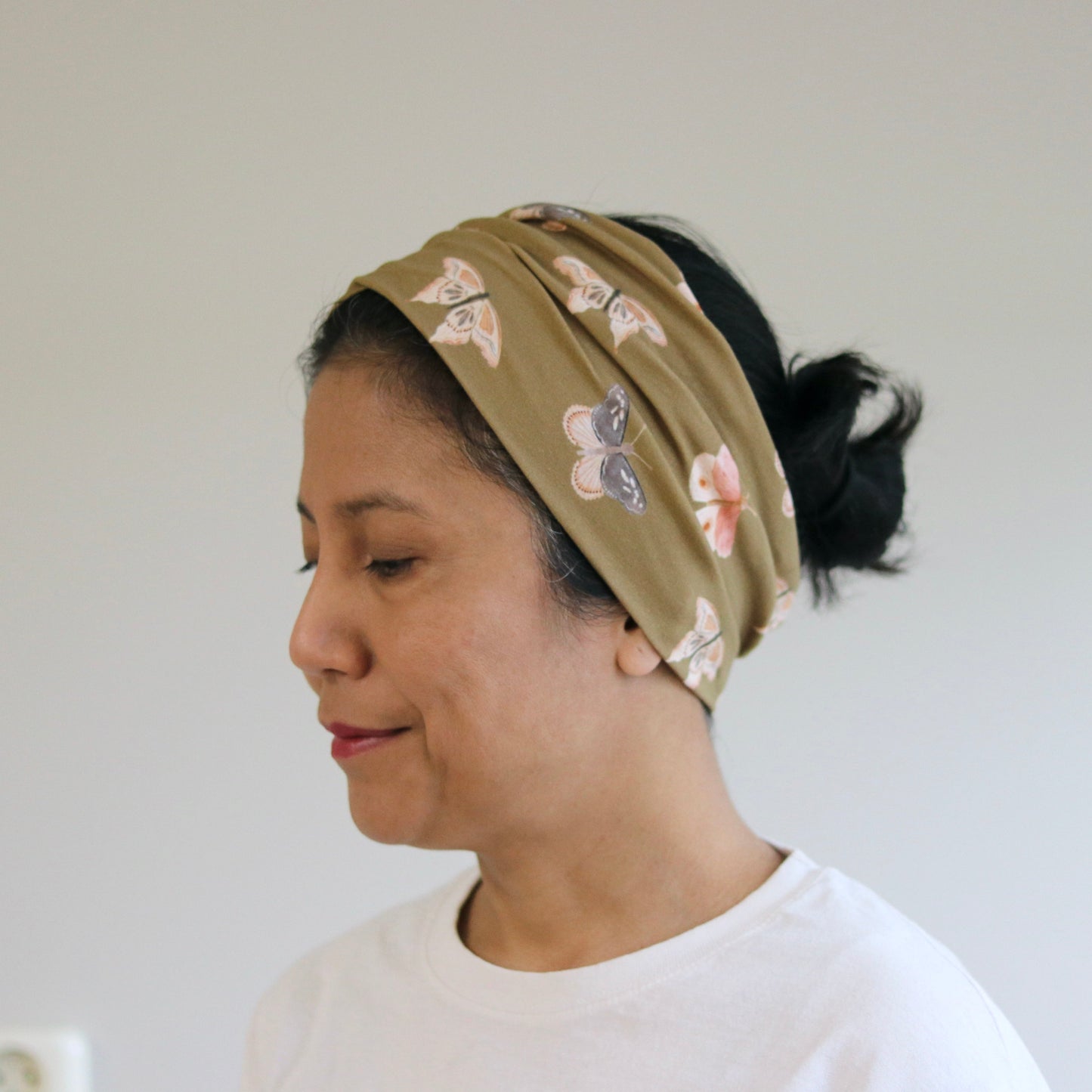 Woman wearing a moss green headband with floral patterns against a plain background