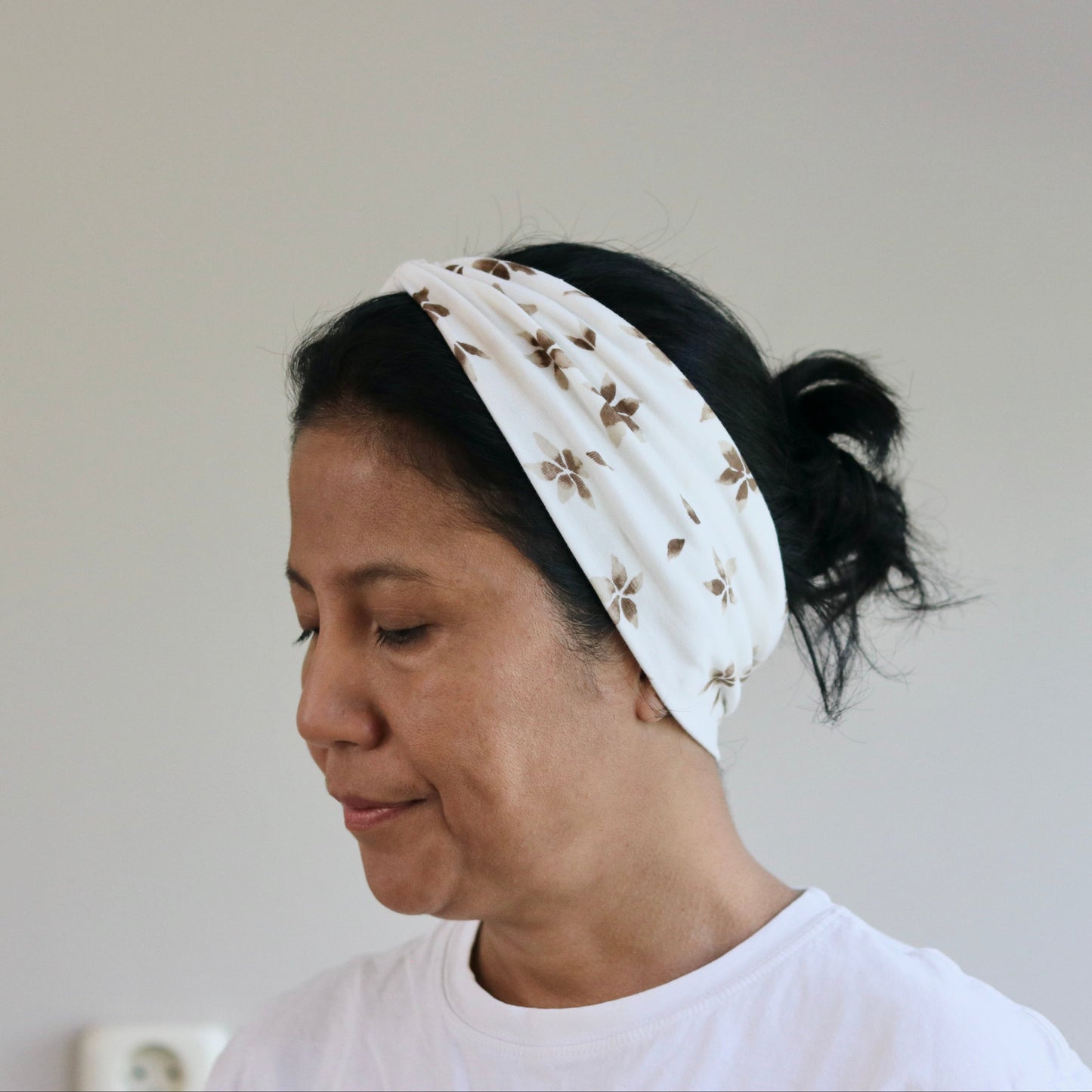 Woman wearing a white headband with a pattern against a plain background