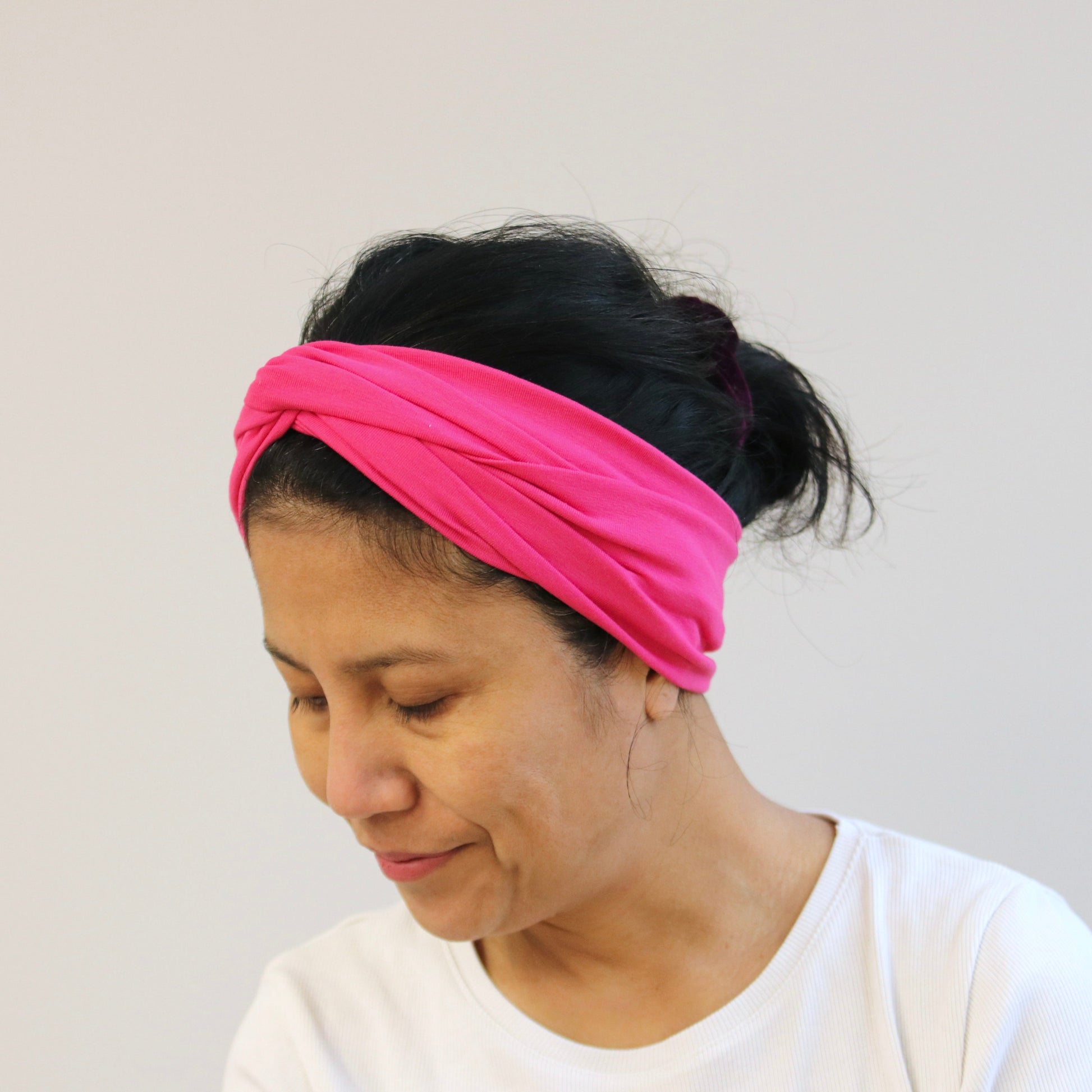 Woman wearing a fuchsia- pink headband against a plain background