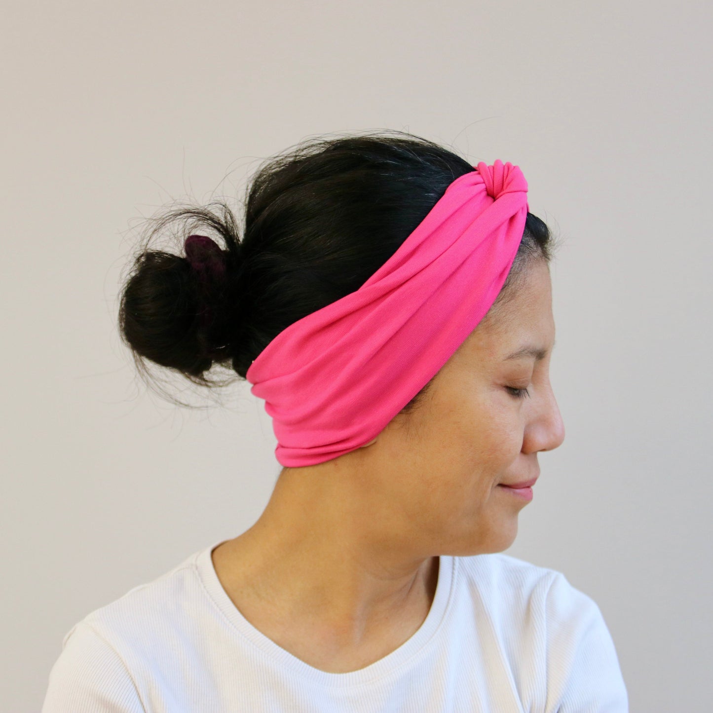 Woman wearing a fuchsia- pink headband against a plain background