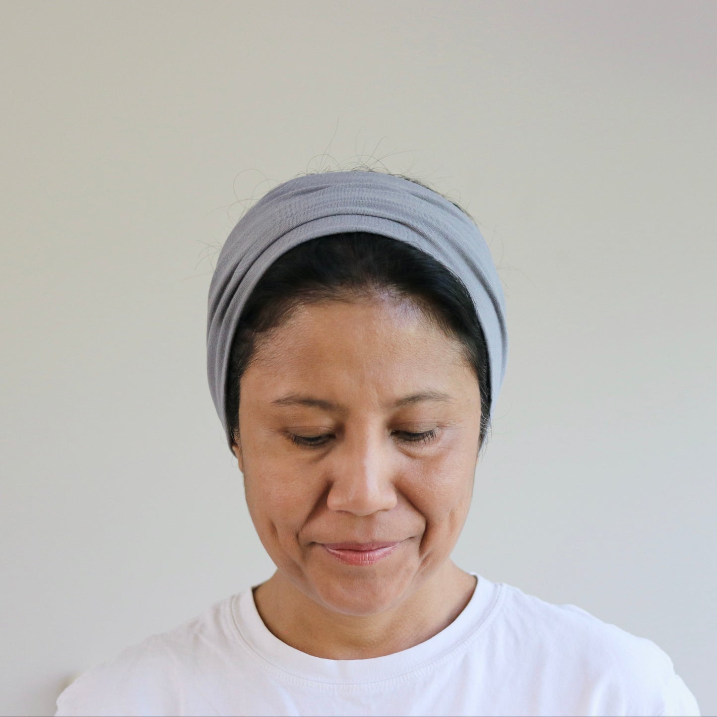 Woman wearing a gray headscarf and white shirt against a plain background