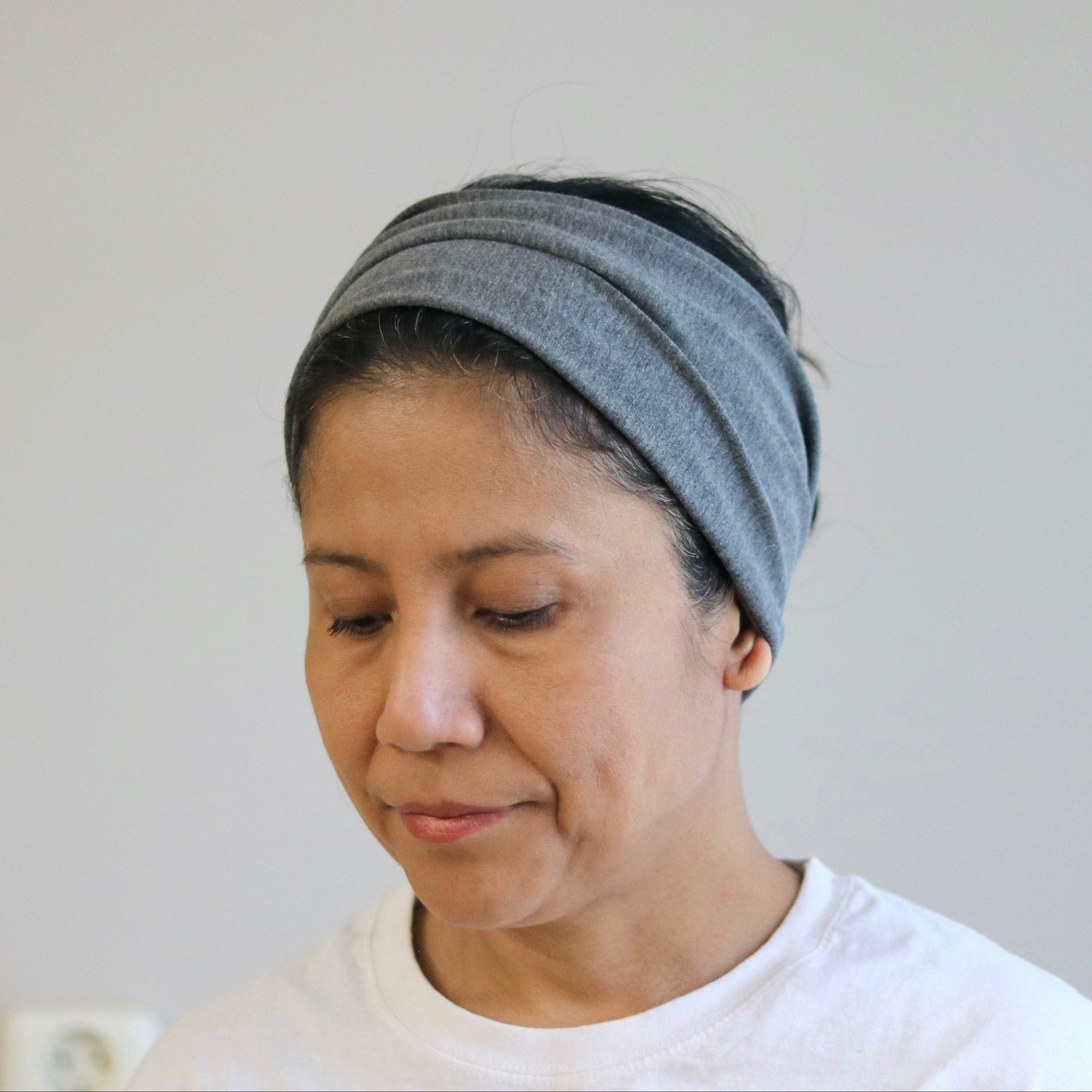 Woman wearing a gray headscarf against a plain background
