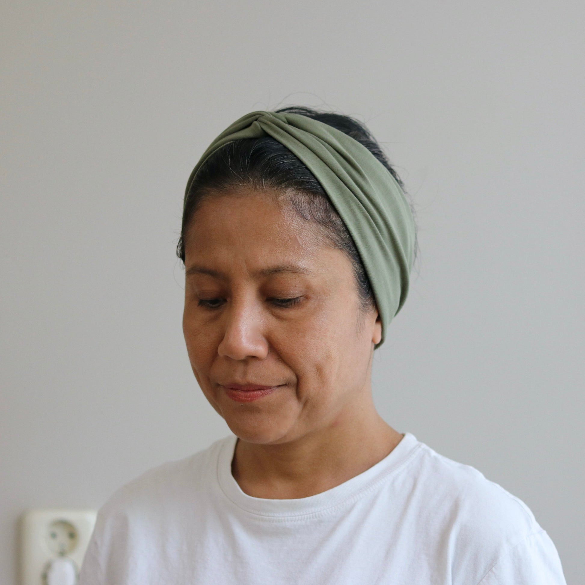 Woman wearing a khaki- green headscarf against a plain background