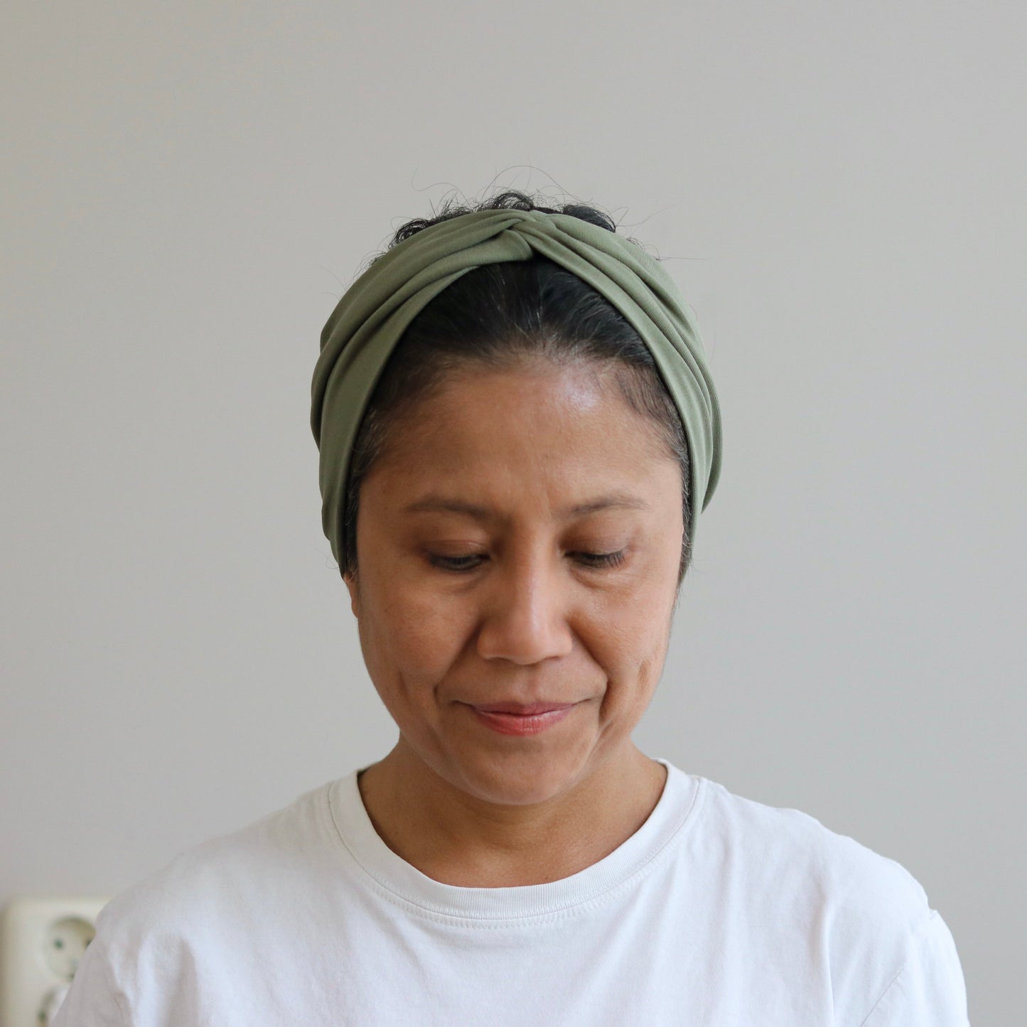 Woman wearing a green headscarf and white shirt against a plain background