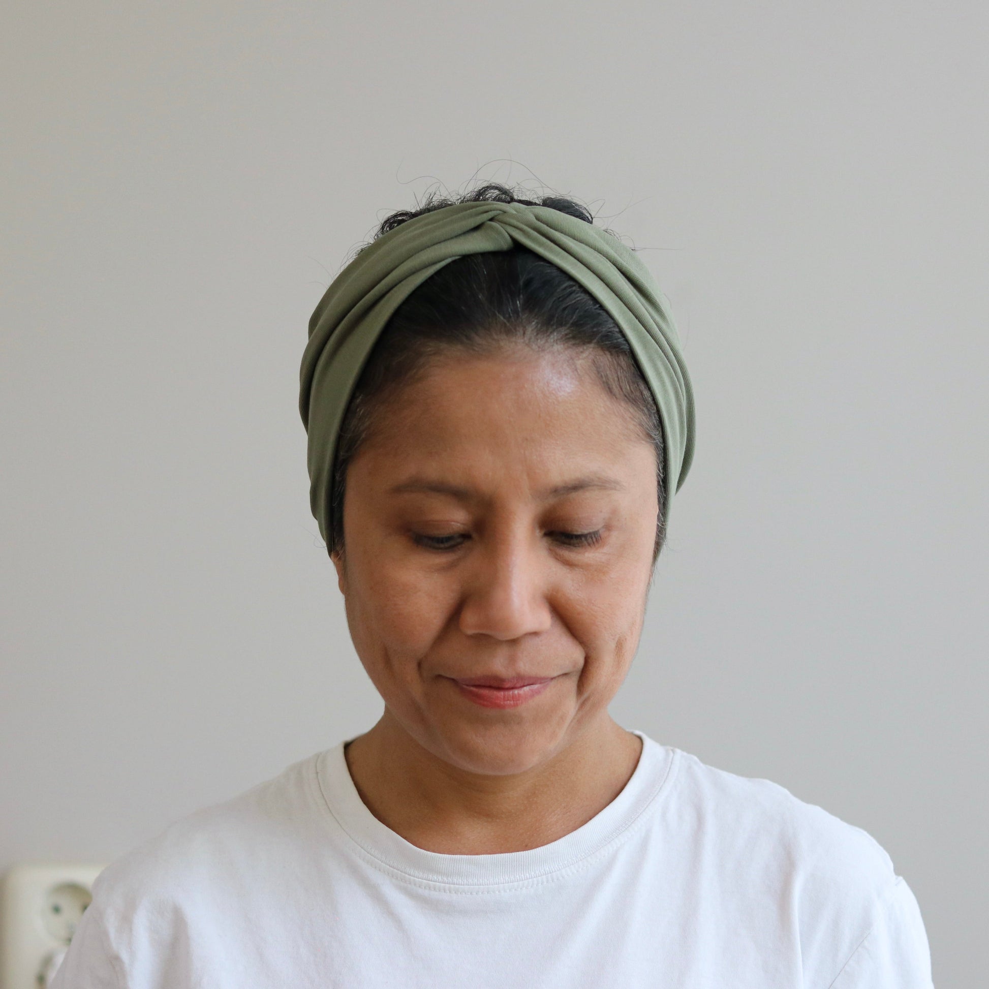 Woman wearing a green headscarf and white shirt against a plain background