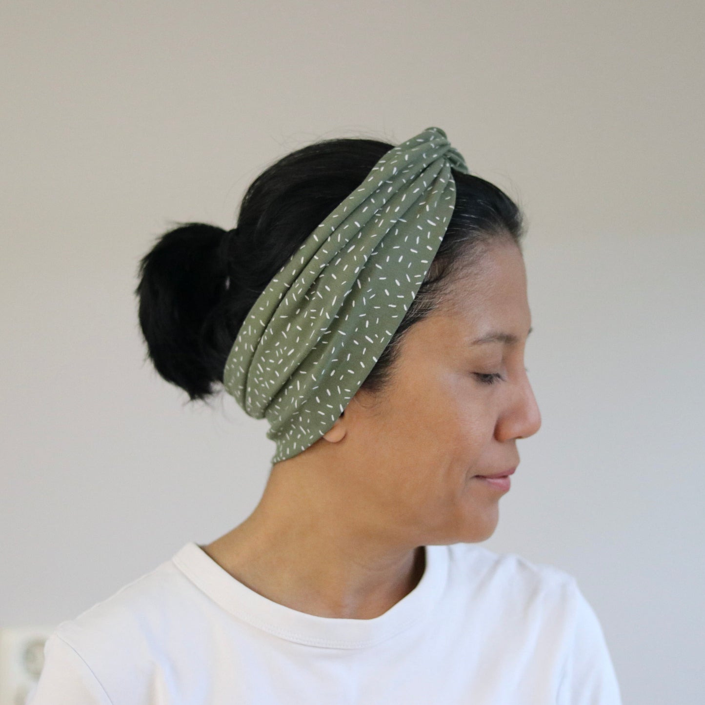 Woman wearing a green polka dot headband against a plain background