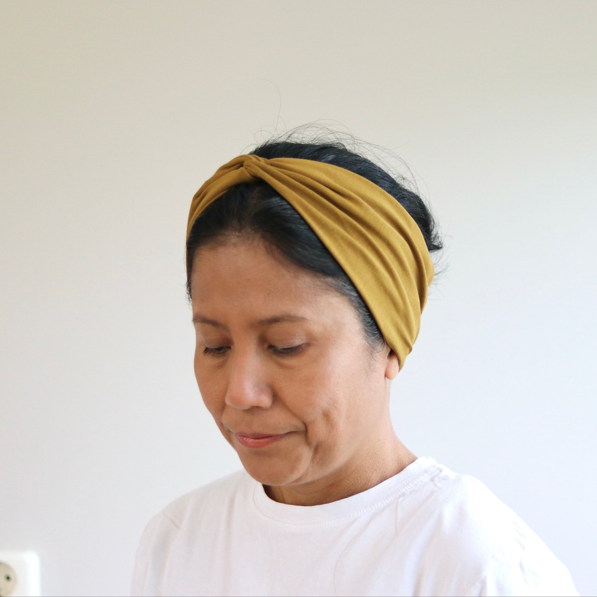 Woman wearing an ocher- brown headscarf against a white background