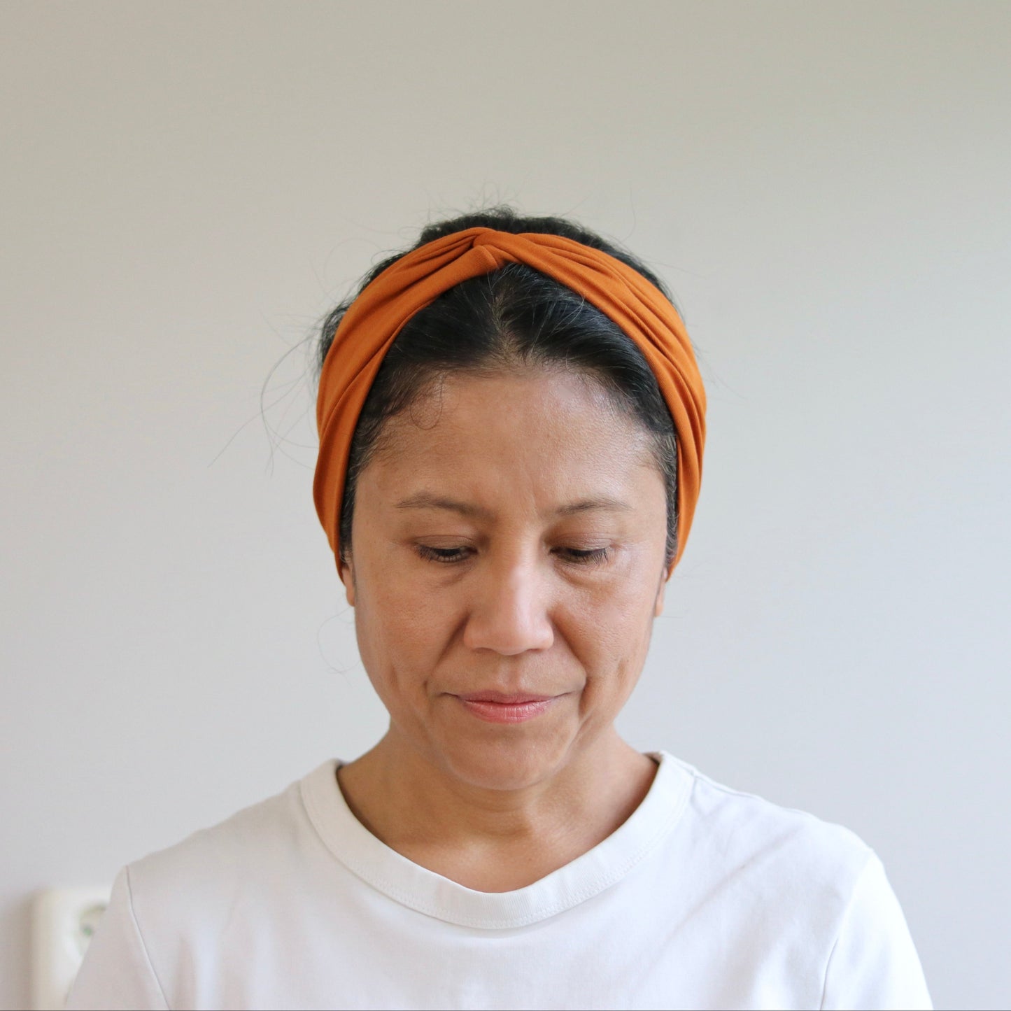 Woman wearing an orange headband against a plain background