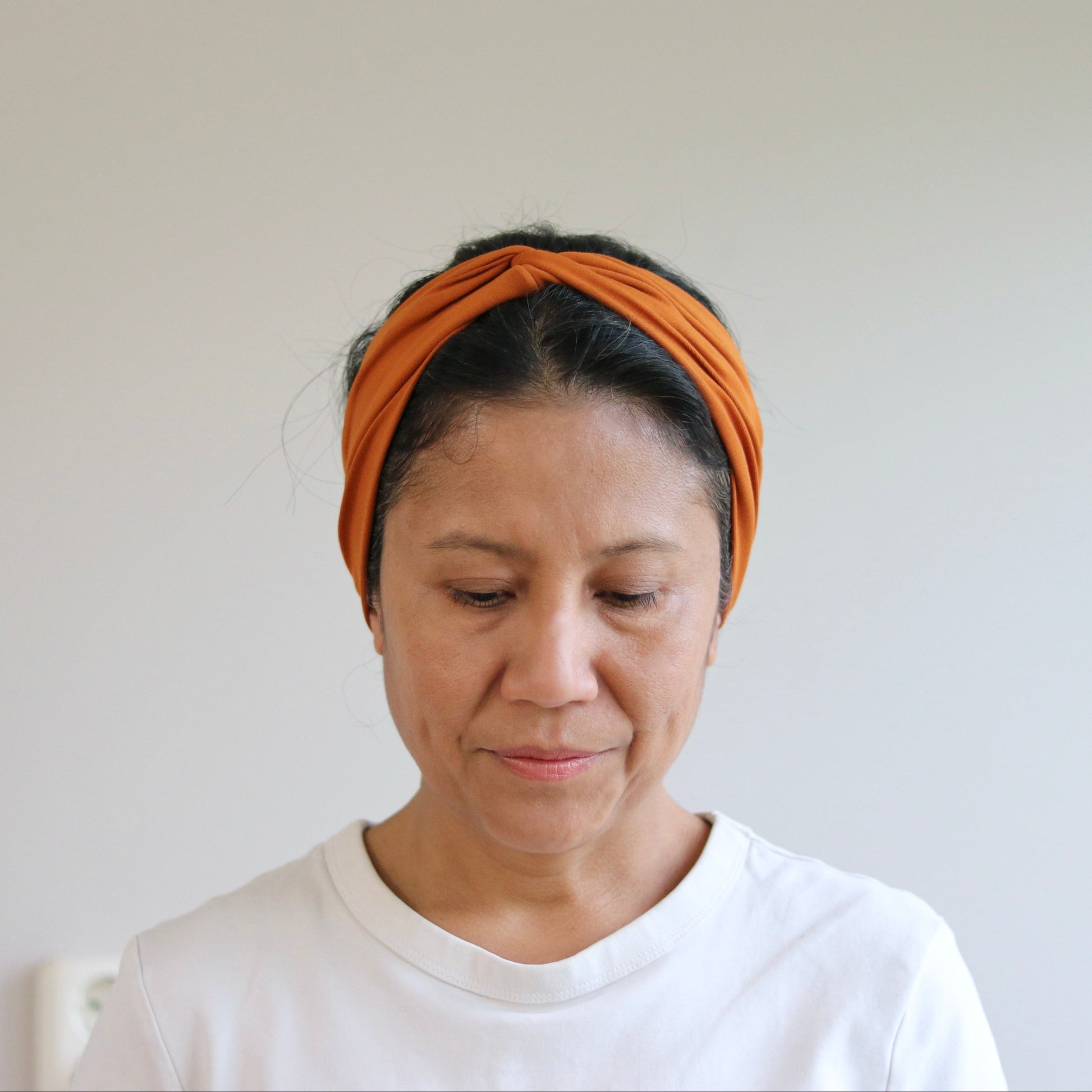 Woman wearing an orange headband against a plain background