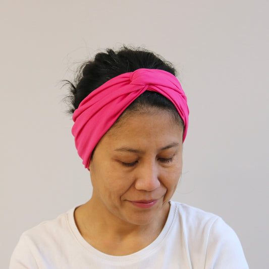 Woman wearing a fuchsia- pink headband against a plain background