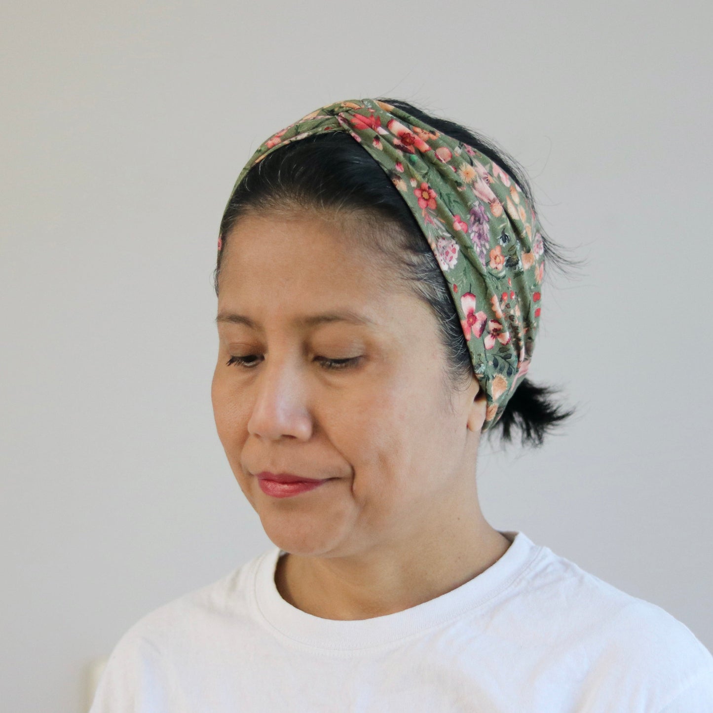 Woman wearing a floral headscarf and white shirt against a plain background