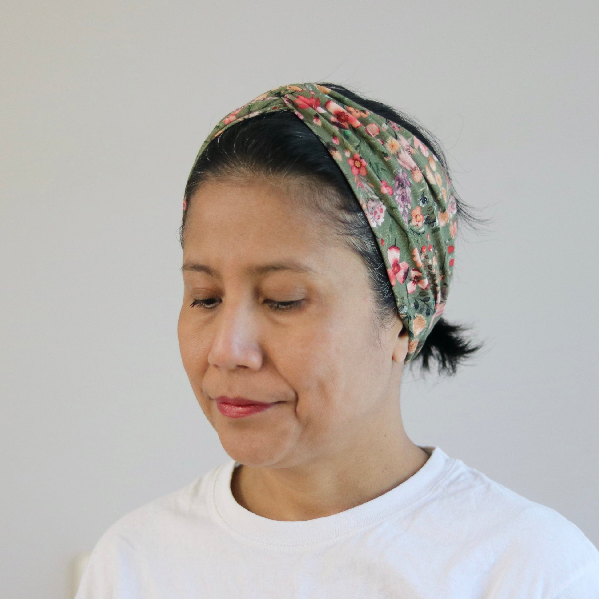 Woman wearing a floral headscarf and white shirt against a plain background