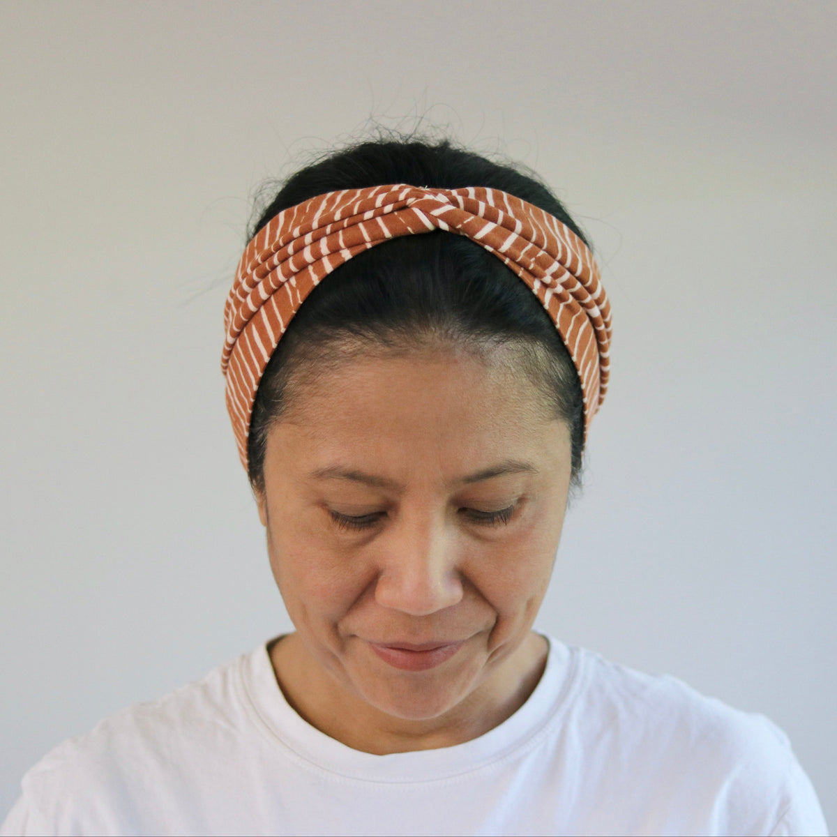 A woman wearing a textured, twisted orange and white patterned headband, looking down in a brightly lit indoor setting.