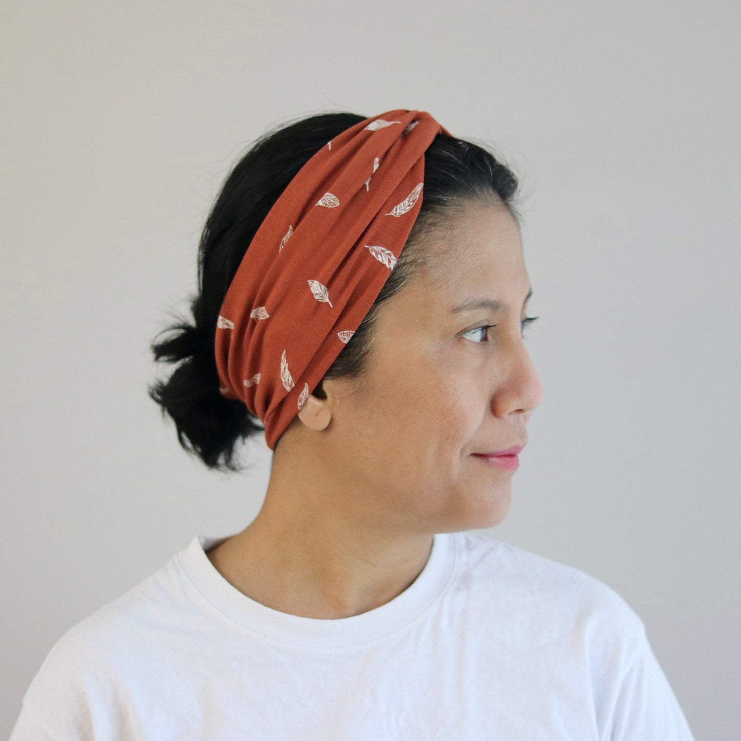 Woman wearing a rust-colored headband with white patterns against a plain background
