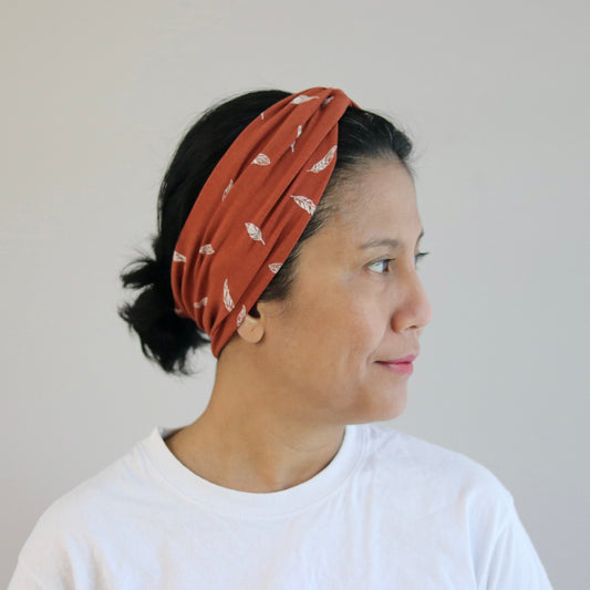Woman wearing a rust-colored headband with white patterns against a plain background