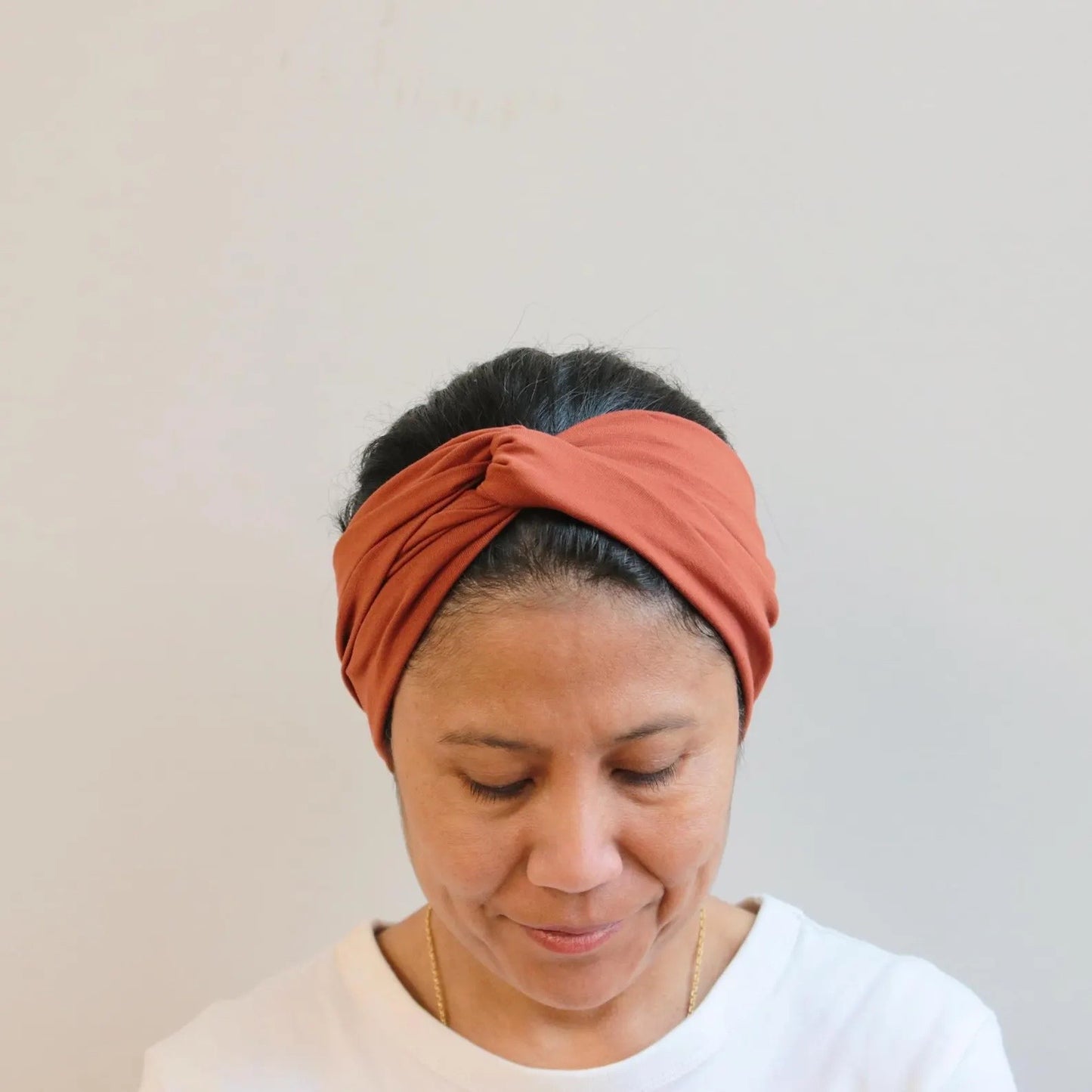 Woman wearing a rust-colored headband against a plain background