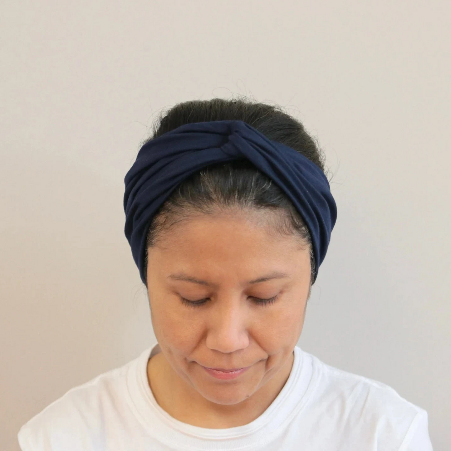 Woman wearing a navy blue headband against a beige background